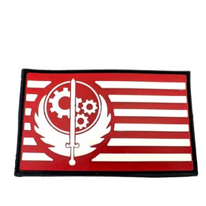 Peut inclure: Patch rouge et blanc avec un symbole blanc d'une épée et d'engrenages avec des ailes. Le symbole est sur un fond rouge avec des rayures blanches.