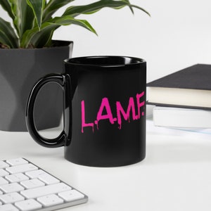 Puede incluir: Taza de café de cerámica negra con un gráfico rosa goteante "L.A.M.F.".