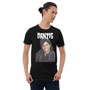 May include: Black t-shirt with a white graphic of a man with long hair wearing a leather jacket. The graphic has the text "DANZIG" above it.