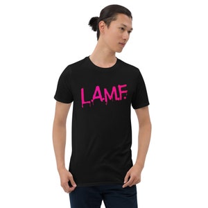 Puede incluir: Una camiseta negra con un gráfico rosa que dice "LAMF". El gráfico está goteando, como si estuviera pintado con una sustancia húmeda.