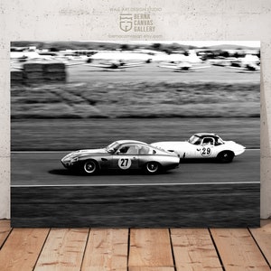 May include: Black and white photograph of two vintage racing cars speeding down a track. The car in the foreground is number 27 and the car in the background is number 29.