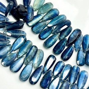 May include: A strand of blue kyanite gemstone beads in a teardrop shape. The beads have a shimmery, iridescent finish.