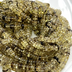 May include: A strand of light green and brown faceted gemstone beads. The beads are round and have a slightly irregular shape. The beads are strung on a clear thread.