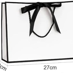 May include: A white gift bag with black trim and a black ribbon bow. The bag is 27 cm wide, 21 cm tall, and 10 cm deep (approximately 10.6 inches wide, 8.3 inches tall, and 3.9 inches deep). The bag has black rope handles.