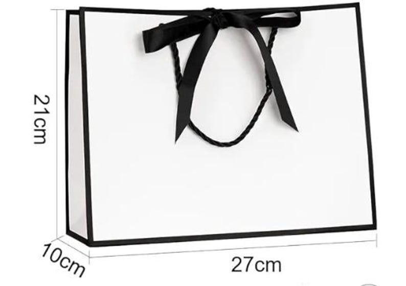 May include: A white gift bag with black trim and a black ribbon bow. The bag is 27 cm wide, 21 cm tall, and 10 cm deep (approximately 10.6 inches wide, 8.3 inches tall, and 3.9 inches deep). The bag has black rope handles.