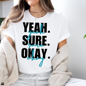 May include: White t-shirt with black text that reads "Yeah. Sure. Okay." The text is in a bold, playful font with the word "Okay" written in a blue cursive font.