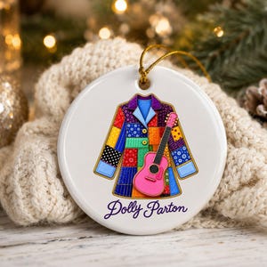 May include: A round white ceramic ornament featuring a colorful patchwork jacket illustration with a bright pink acoustic guitar overlaid on the front. The text Dolly Parton is printed in purple script at the bottom of the ornament.