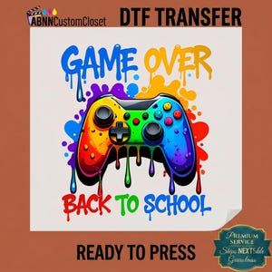 May include: A DTF transfer sheet featuring a colorful video game controller graphic with a paint splatter effect. The text reads GAME OVER at the top and BACK TO SCHOOL at the bottom. The design includes vibrant blue, yellow, red, and green hues.