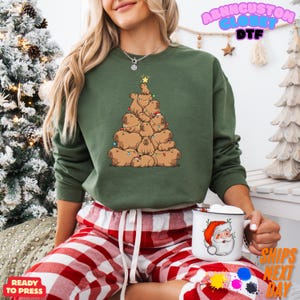 May include: Green sweatshirt featuring a Christmas tree design made of capybaras. The capybaras are brown and arranged in a tree shape, with a star on top. The sweatshirt has long sleeves and a crew neck. The text "ABNNCUSTOM GLOBE DTF" is visible.