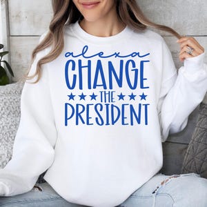 May include: White sweatshirt with blue text that reads "Alexa Change the President" with five stars on either side of "the".