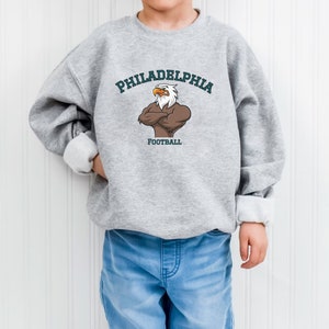 May include: A gray sweatshirt with a green and white eagle graphic and the text "PHILADELPHIA FOOTBALL" on the front.