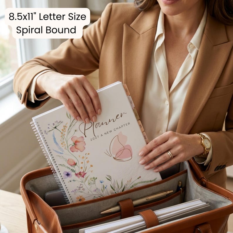 May include: An 8.5x11 inch letter size spiral bound planner with a white cover featuring a watercolor floral design, a pink butterfly outline, and the text Planner 2027 A New Chapter, placed inside a brown leather bag with internal pockets.