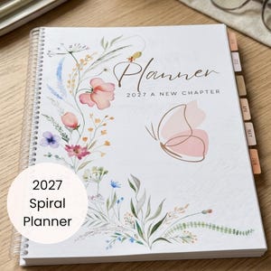 Puede incluir: Una agenda 2027 de espiral blanca con una delicada ilustración floral en acuarela a la izquierda y una mariposa de líneas minimalistas a la derecha. El texto de la portada dice Planner 2027 A NEW CHAPTER. Incluye pestañas laterales mensuales.