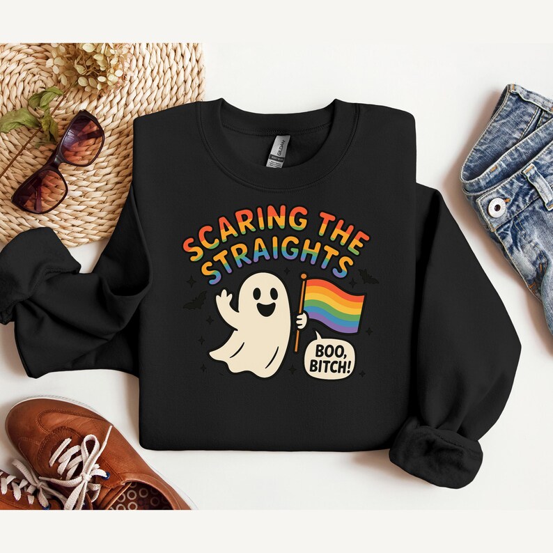 May include: Black crewneck sweatshirt with the text "Scaring the Straights" in rainbow colors. A cartoon ghost waves a hand and holds a rainbow flag. The phrase "Boo, Bitch!" is below the flag.