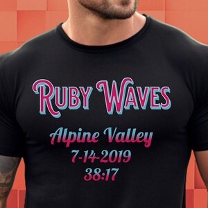 May include: Black t-shirt with pink and blue text that reads "Ruby Waves" "Alpine Valley" "7-14-2019" "38:17"