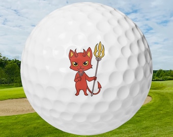 May include: A white golf ball with a red cartoon devil holding a trident. The devil has a red tail and is wearing a gold necklace.