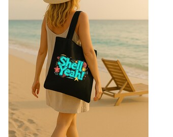 May include: A black tote bag featuring the text "Shell Yeah!" in a vibrant, stylized design. The bag is carried by a person walking on a sandy beach near the sea. A straw hat and a deckchair are also visible.