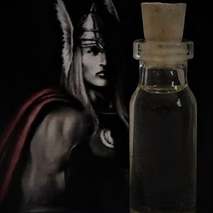 Puede incluir: Una pequeña botella de vidrio transparente con un tapón de corcho, llena de un líquido amarillo claro. Detrás de la botella hay una pintura de una mujer con casco alado y capa roja, sobre un fondo negro.