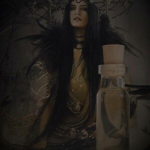 May include: A clear glass bottle with a cork stopper, filled with a dark liquid. The bottle is in front of a dark background with a woman in the background.