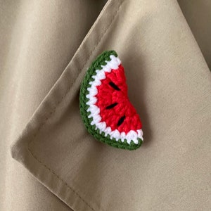 Könnte beinhalten: Eine gehäkelte Wassermelonen-Scheiben-Brosche in Rot, Grün und Weiß. Die Brosche ist ein süßes und skurriles Accessoire für eine Jacke oder Tasche.