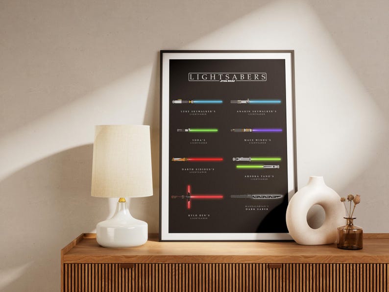 May include: Framed black poster featuring various lightsabers from Star Wars. The poster includes the text "LIGHTSABERS STAR WARS" at the top. A white lamp and a white vase are on a wooden surface.