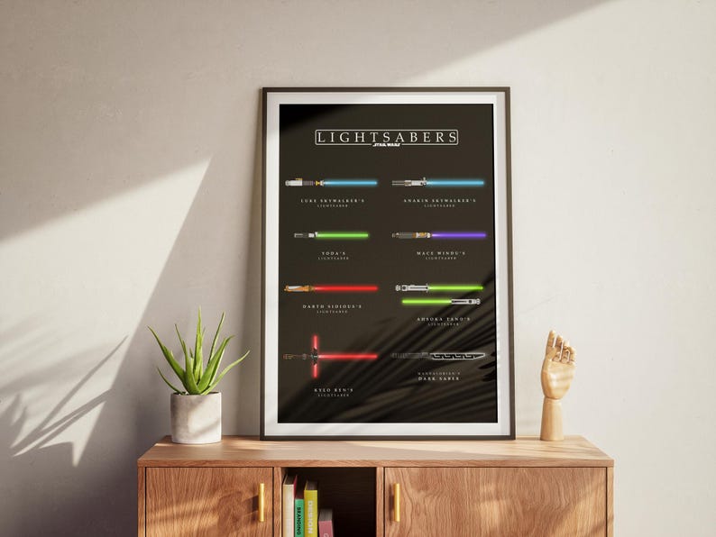 May include: A framed poster displaying lightsabers from Star Wars, each identified with a name. The lightsabers are shown in their distinctive colours, such as blue, green, red, and purple, set against a dark backdrop. The poster is on a wooden cabinet.