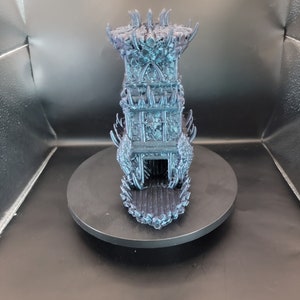 May include: A 3D printed miniature tower with a dark blue and black color scheme. The tower has a pointed roof and intricate details, resembling a gothic or fantasy style.