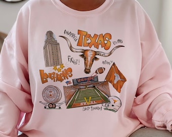 May include: Pink sweatshirt with a graphic print of the University of Texas Longhorns logo, mascot, and stadium. The graphic includes the words "University of Texas", "Fight!", "Longhorns", "Austin, Tx", "Revo", "Est 1883", "Hook 'em Horns", and "DKR Stadium".