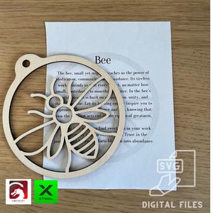 May include: A wooden cutout of a bee with a circle around it. The bee is in the centre of the circle. The bee is brown and has black stripes. The circle is also brown. The text "Bee" is written above the bee. The text below the bee reads: "The bee, small yet mighty, teaches us the power of dedication, community, and abundance. Its tireless work reminds us that every small contribution to something good is built on hope. Let its buzzing energy inspire you to approach life with diligence and knowing that even the smallest acts can create ripples of greatness. Find sweet success in your work. Trust in the efforts to bloom into abundance."