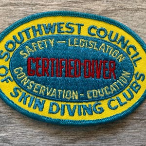 May include: Embroidered patch with a yellow border and a blue oval center. The text "SOUTHWEST COUNCIL OF SKIN DIVING CLUBS" arches around the top and bottom. The center reads "CERTIFIED DIVER" in red.