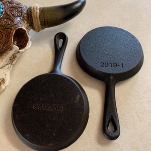 May include: Two cast iron mini skillets, one with the word "Casserole" on the bottom and the other with the date "2019-1".