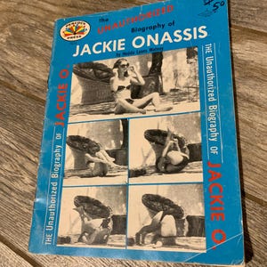 Puede incluir: Un libro de bolsillo vintage titulado "The Unauthorized Biography of Jackie Onassis" de Hedda Lyons Watney. La portada es azul con una foto de Jackie O. y otras imágenes. El logotipo de Peacock Press es visible.