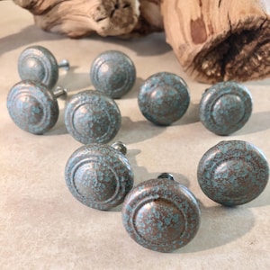 May include: A collection of eight round cabinet knobs featuring a textured, mottled finish in shades of teal and copper. Each knob has a raised circular center detail and a metal mounting screw extending from the back for attachment to furniture.