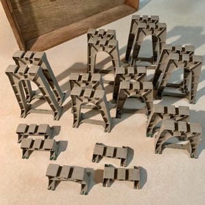 May include: A collection of gray plastic sawhorse supports in various sizes and shapes. The supports are designed to hold up materials during construction or woodworking projects. Some are A-frame style, while others are shorter, rectangular blocks.