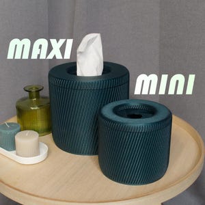 May include: Two tissue box holders, one labeled "maxi" and the other "mini". Both are dark green with a ribbed texture. The larger one has a white tissue box inside.