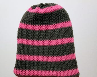 Puede incluir: Un gorro de punto con rayas horizontales. El gorro es principalmente gris oscuro con rayas rosa brillante. El gorro está hecho de un hilo suave y texturizado y tiene una parte superior redondeada. El gorro es un accesorio de invierno.