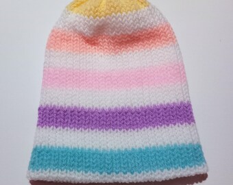 Puede incluir: Un gorro tejido a mano con rayas horizontales en colores pastel. Las rayas incluyen blanco, amarillo, rosa, morado y turquesa. El gorro está hecho de hilo suave y es adecuado para el clima frío.