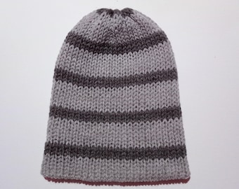 Puede incluir: Un gorro de punto a rayas grises y marrones. El gorro presenta rayas horizontales de diferentes tonos de gris y marrón. El gorro está hecho de un material de punto suave y está diseñado para ajustarse perfectamente a la cabeza.