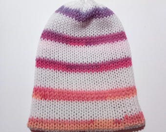 Puede incluir: Un gorro tejido con rayas horizontales blancas, moradas, rosas y naranjas. El gorro está hecho de hilo suave y es adecuado para el clima frío. El gorro es un accesorio elegante.