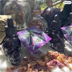 May include: Dark skull-shaped glass bottles with black droppers and tags reading "Dead Man's Bells." The bottles contain a dark liquid, with dried flowers and other apothecary items in the background. The tags are purple with a floral design.