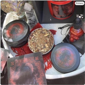 Puede incluir: Una variedad de artículos espirituales, incluyendo latas negras con texto rojo y blanco y un diseño de silueta. Una lata está abierta, revelando una mezcla de hierbas. También se ve una botella con forma de calavera y una baraja de cartas.