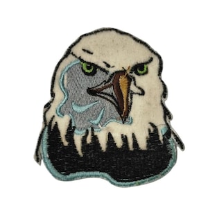 May include: Embroidered patch featuring an eagle's head. The patch has a white head with green eyes, a brown beak, and a light blue and black outline. The eagle's head is a detailed, stylized design.