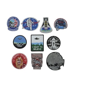 May include: A set of ten embroidered iron-on patches featuring space, sci-fi, and pop culture themes. The patches include images of spaceships, astronauts, aliens, and the Death Star. The patches are circular and have a variety of colours, including red, blue, green, and black.
