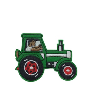 Peut inclure: Tracteur vert avec une bande blanche et des roues rouges. Une personne conduit le tracteur.