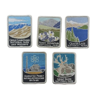 May include: Set of six embroidered patches featuring national parks and landmarks. The patches are rectangular and have a white border. The patches feature images of Great Sand Dunes National Park and Preserve, Rocky Mountain National Park, Crater Lake National Park, Manhattan Project National Historical Park, Great Basin National Park, and a stylised image of an atom.