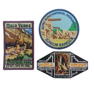 May include: Three embroidered patches featuring Mesa Verde National Park. The first patch is a rectangular patch with a purple border and a depiction of the park's landscape. The second patch is a round patch with a blue border and the text "Aztec Ruins National Monument Junior Ranger". The third patch is a black diamond-shaped patch with the text "Mesa Verde World Cultural Heritage Site National Park".