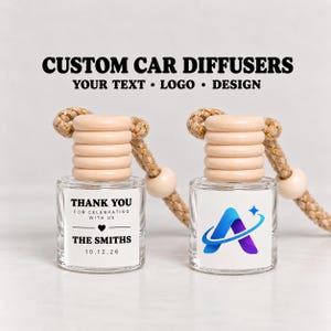 May include: Two small glass car diffusers with light wood ribbed caps and tan braided hanging cords. One bottle features black text reading THANK YOU FOR CELEBRATING WITH US THE SMITHS 10.12.26, while the other displays a blue and purple letter A logo.