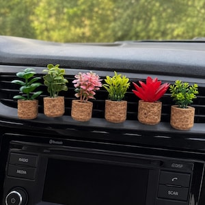 May include: Six miniature artificial plants in small cylindrical cork pots arranged in a row. The plants include green leafy sprigs, a pink-toned plant, and a vibrant red succulent. Each cork pot has a textured, granular surface appearance.