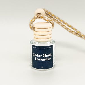 May include: A small glass bottle with a wooden cap and a string for hanging. The bottle contains a clear liquid and has a label that reads "Cedar Musk Lavender" and "8 ml".