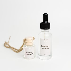 May include: Two clear glass bottles with black caps and labels that read "bamboo + coconut". One bottle has a dropper, the other has a wooden cap and a jute string. The bottles are on a white background.
